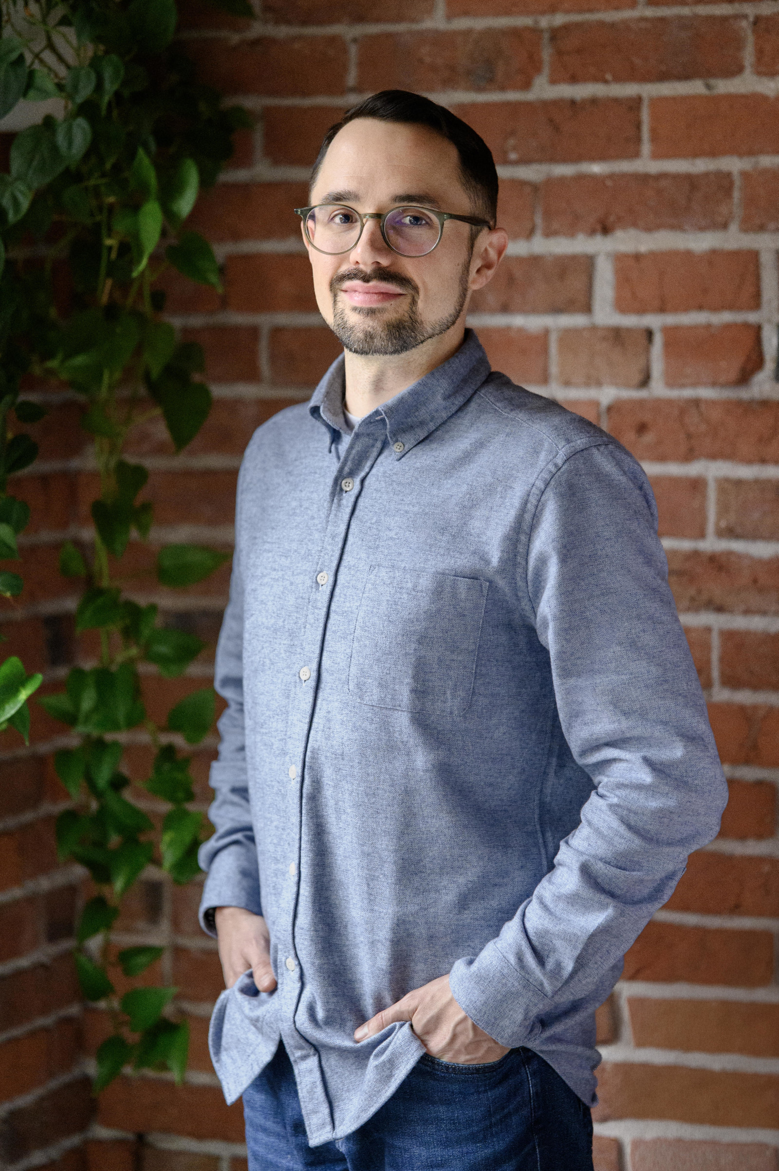 Justin Everett in an untucked blue dress shirt against an exposed brick background.